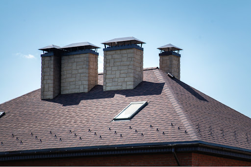 Several chimneys come out of a roof. There is also roof ventilation.